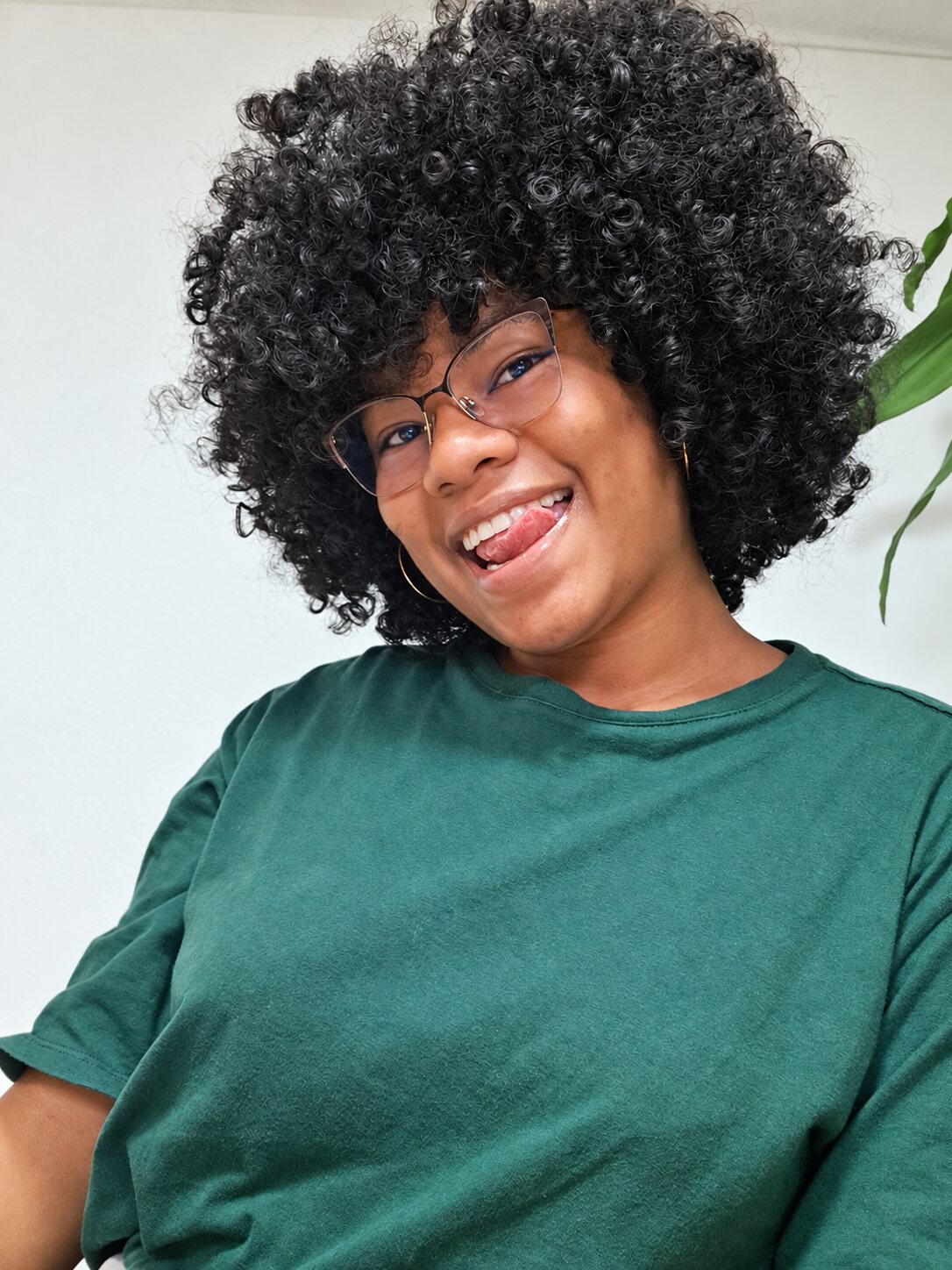 Retrato sonriente con gafas, camiseta verde y cabello rizado con volumen.